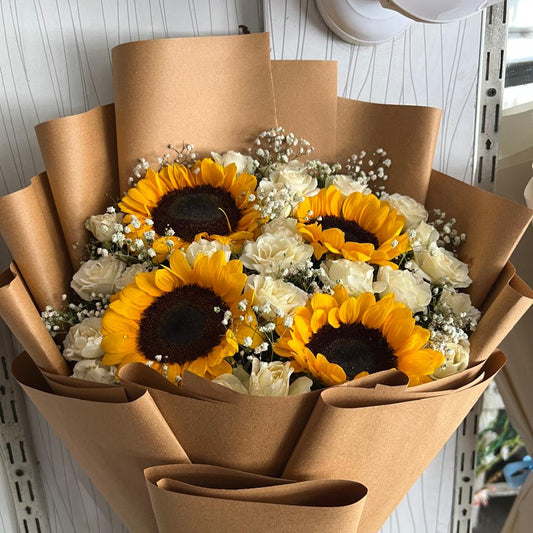 Bouquet of sunflowers and white flowers wrapped in brown paper.