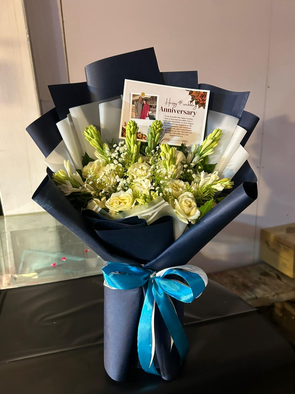 White rose and tuberose anniversary bouquet wrapped in navy with personalized photo card — Moonlit Vow by Flower House Lahore