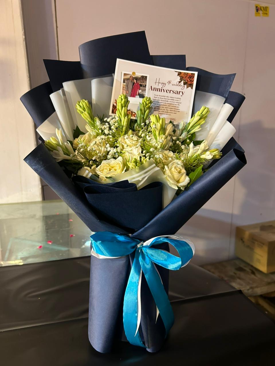 White rose and tuberose anniversary bouquet wrapped in navy with personalized photo card — Moonlit Vow by Flower House Lahore