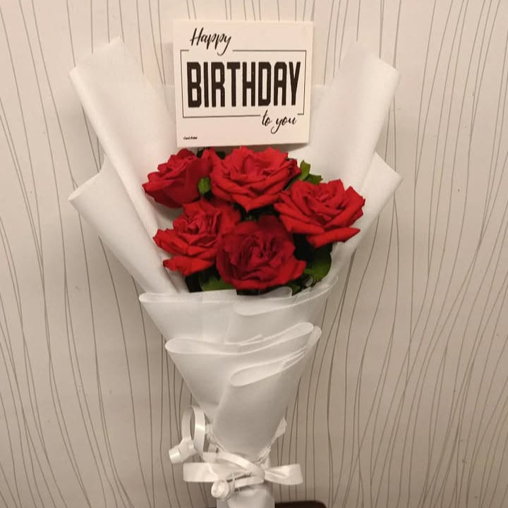 Bouquet of red roses with a 'Happy Birthday' card on a textured wall background