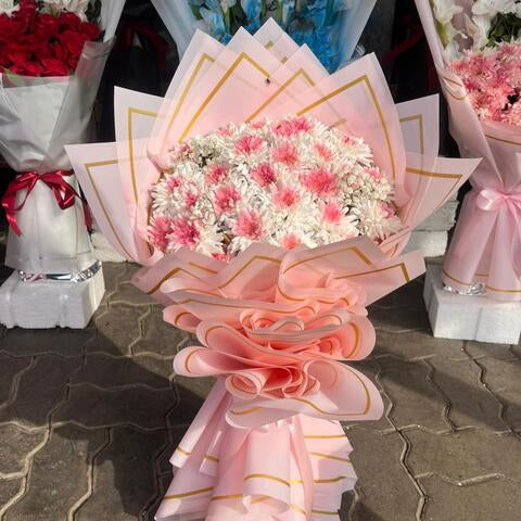 Bouquet of flowers wrapped in pink paper with gold accents on a stone surface.