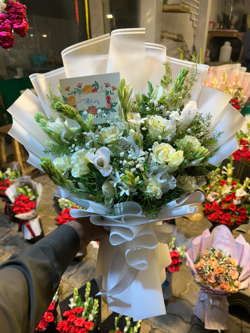 Bouquet of white flowers with a card held by a person in a flower shop.